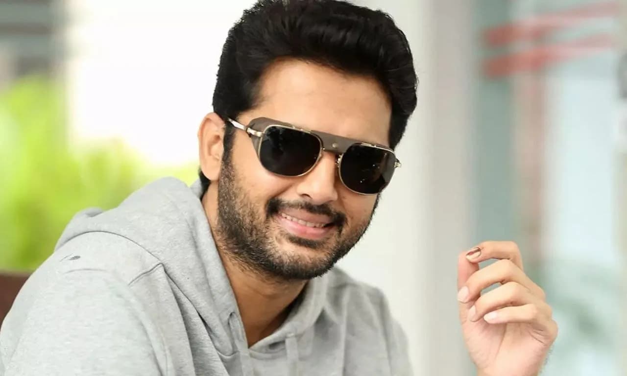 Nithiin in a simple white shirt, looking straight into the lens, no smile. Background blurred.