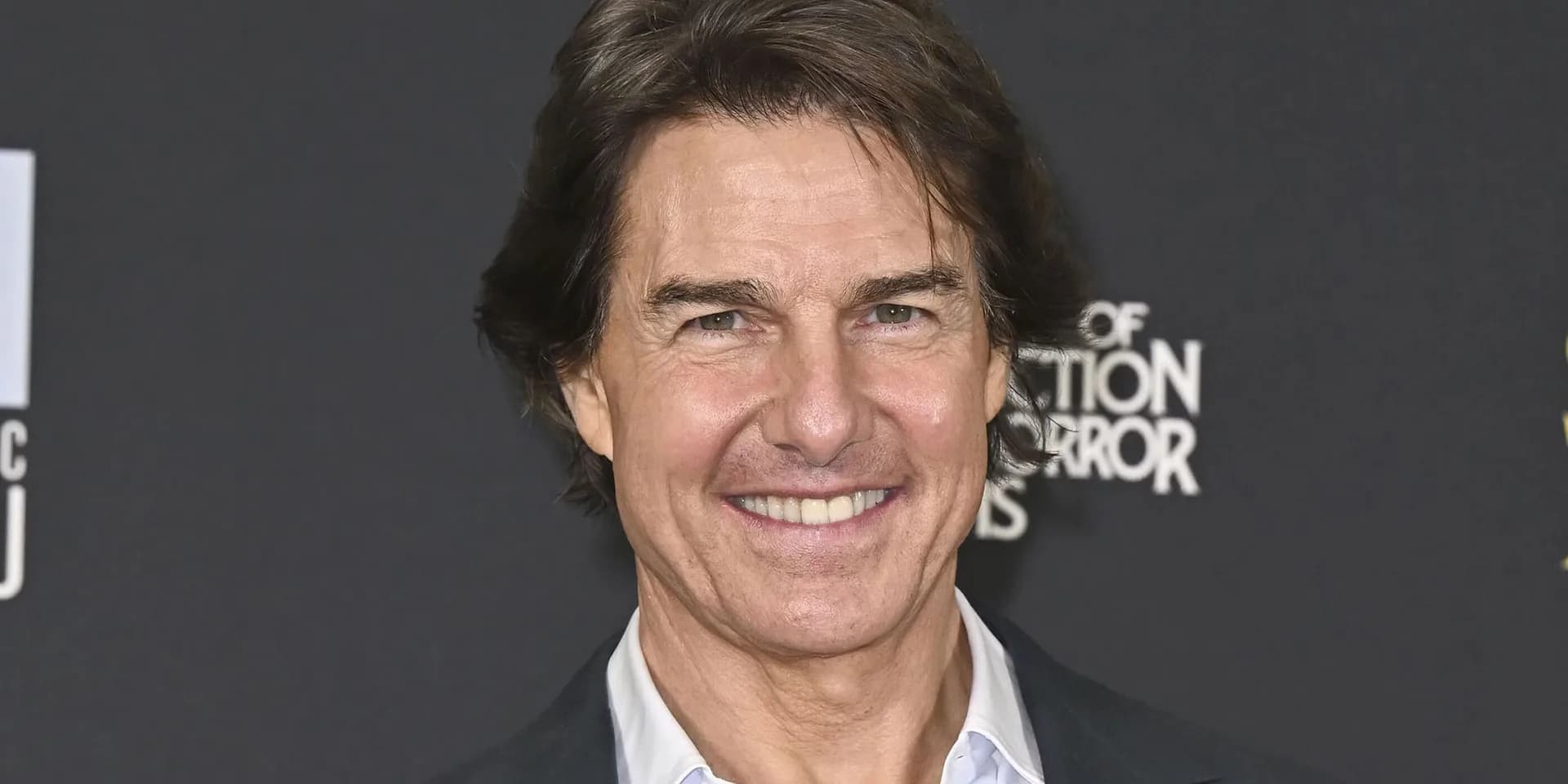 Tom Cruise in a dark suit, standing in front of a city skyline, looking intense.