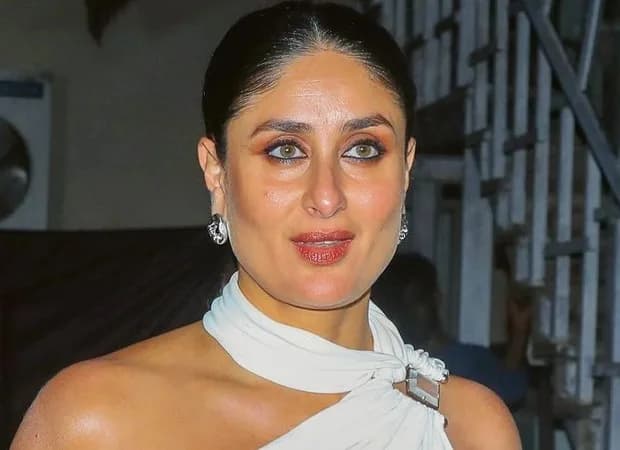 Kareena Kapoor Khan in a racing outfit, holding a helmet, standing against a blurred track backdrop.