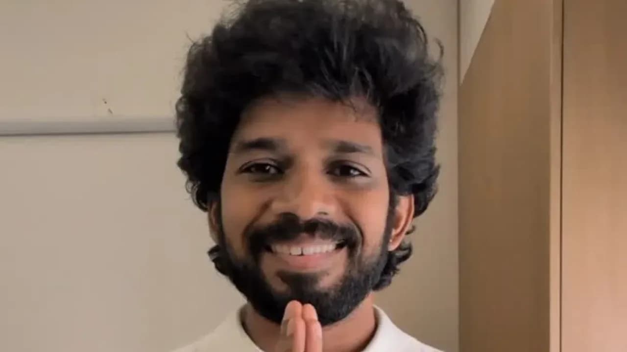 Kumaran Thangarajan standing outside the Bigg Boss house, holding a cash box, looking solemn.