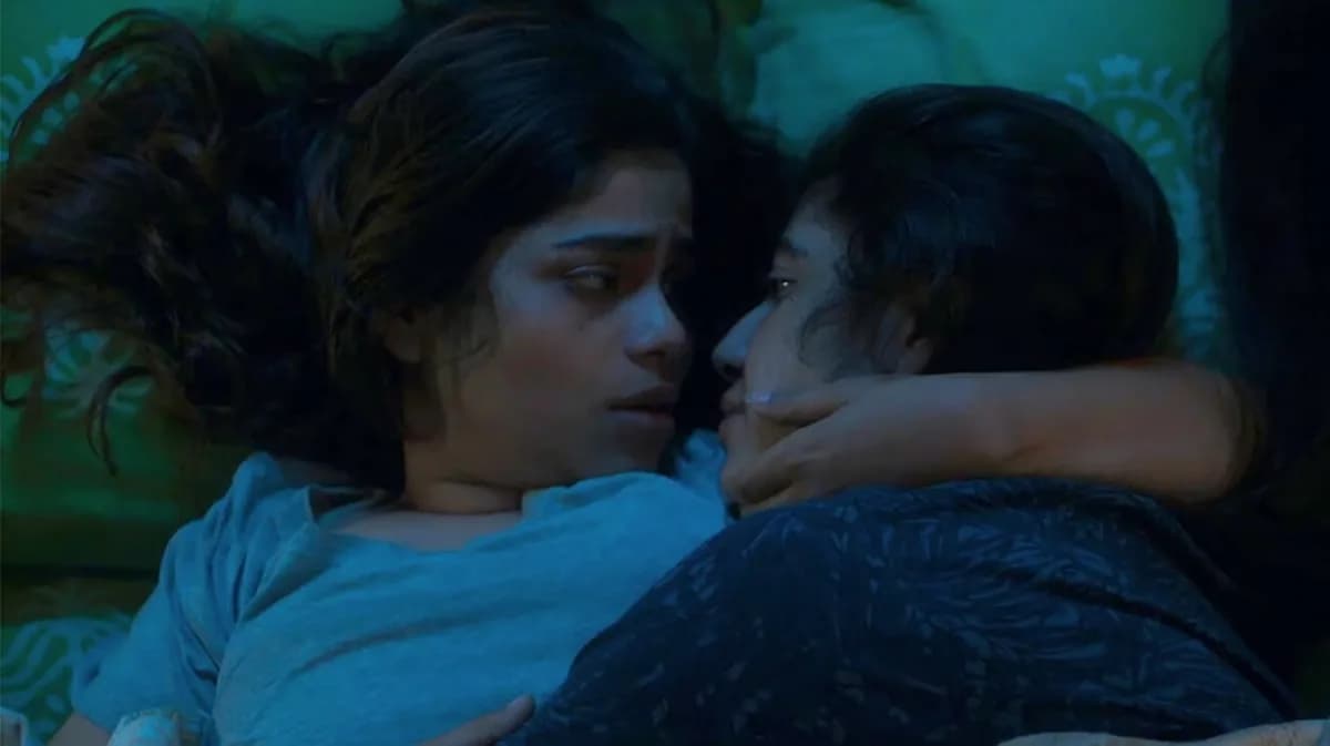 A still from About an Intimate Matter, showing two women sitting close together in a dimly lit room, their faces half in shadow.