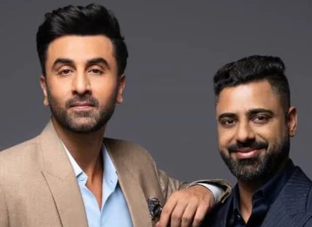 Ranbir Kapoor standing in front of a modern residential development, smiling at the camera.