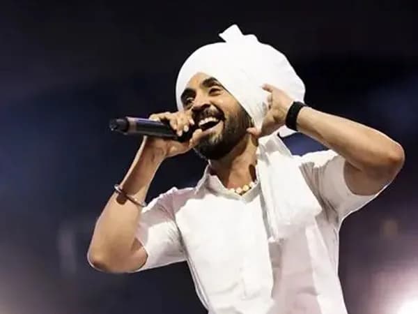 Diljit Dosanjh performing on stage under bright lights, crowd in the background