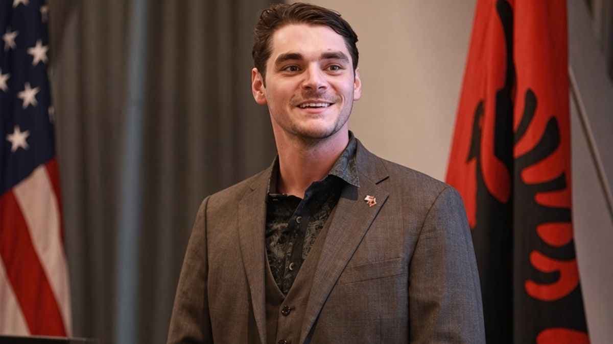 A black-and-white photo of RJ Mitte smiling, mid-speech, holding a microphone.