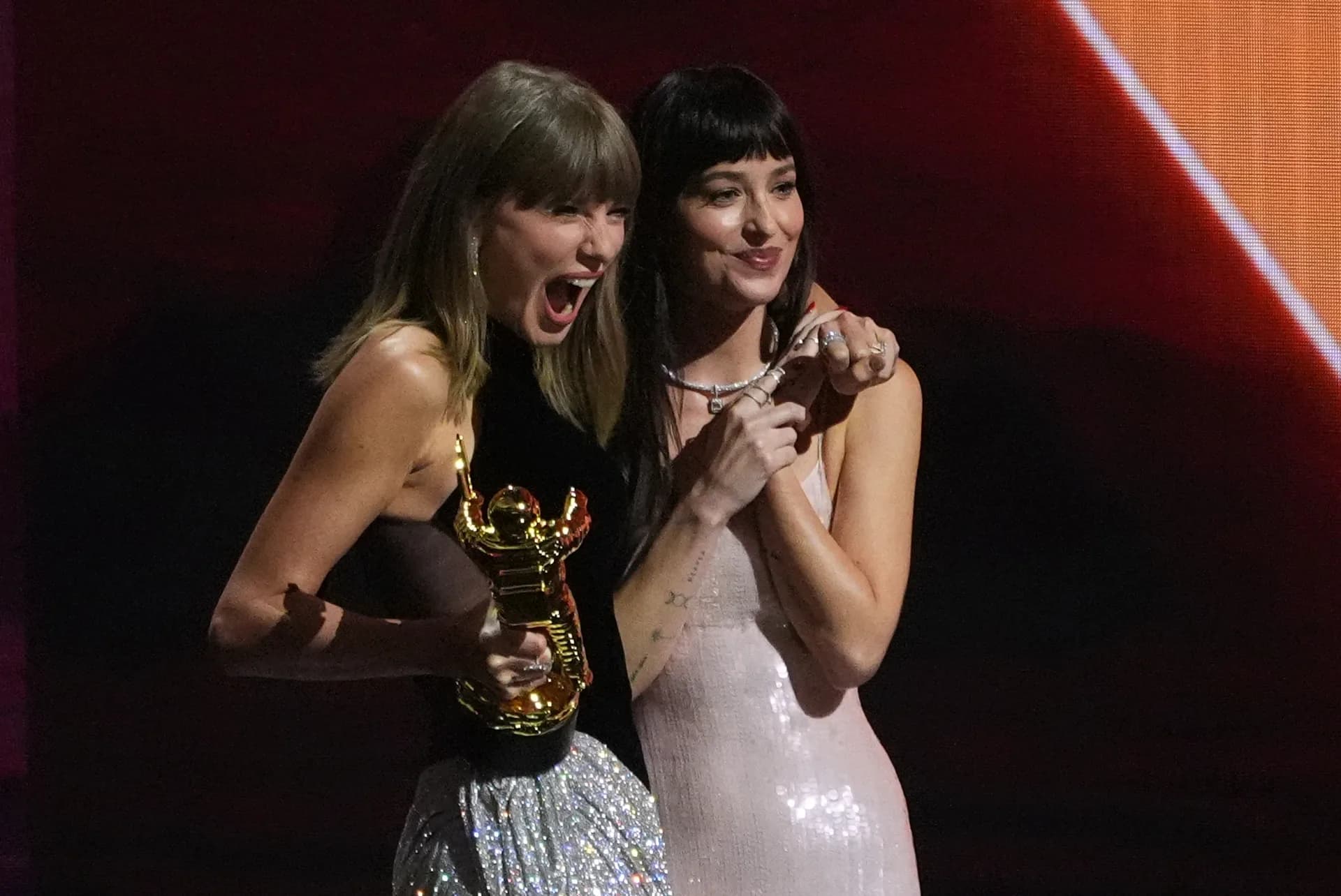 Taylor Swift smiling while holding a VMA trophy, with Dakota Johnson beside her at the 2026 MTV Video Music Awards