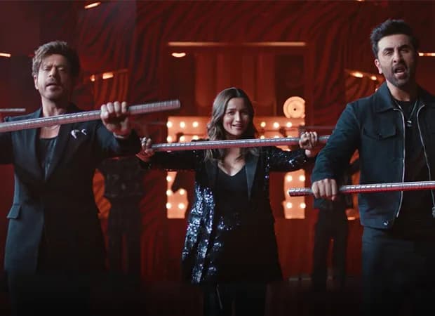 Shah Rukh Khan, Ranbir Kapoor, and Alia Bhatt dancing in a Rungta Steel commercial, holding steel bars, mid-song