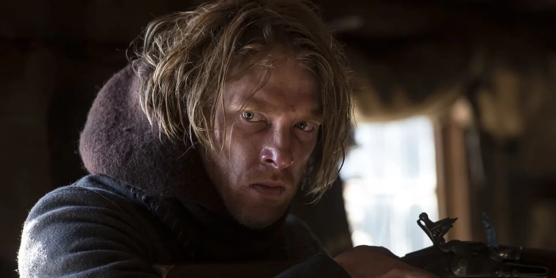 Leonardo DiCaprio as Hugh Glass, lying in snow, face bruised, eyes wide with pain.