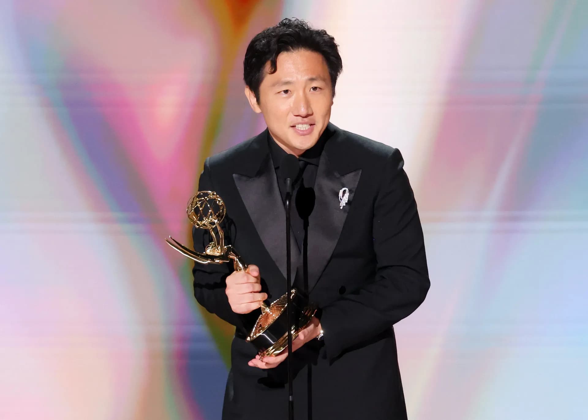 Hiro Murai holding his Emmy statuette on stage after winning Outstanding Directing for a Comedy Series for Widow's Bay.