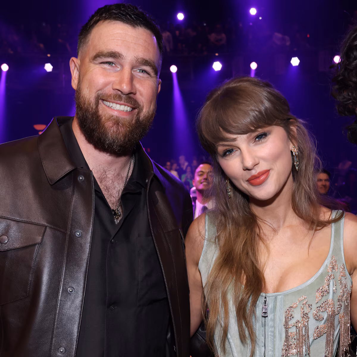 Taylor Swift and Travis Kelce embracing on set of the 'Patient Zero' music video, both smiling.