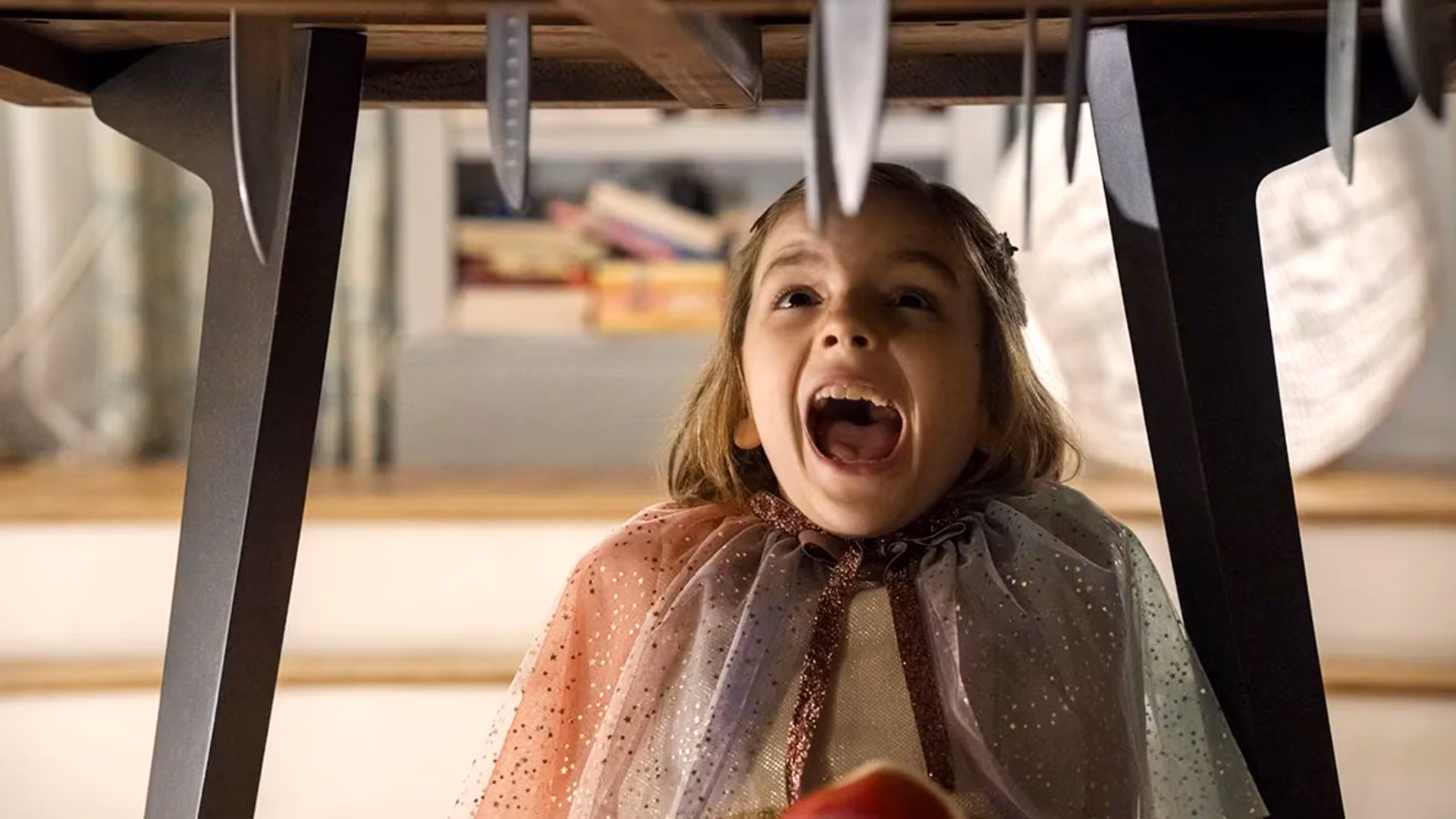Jessica Chastain as a doppelgänger hiding under a kitchen table in a darkened home, lit by a single flickering bulb.