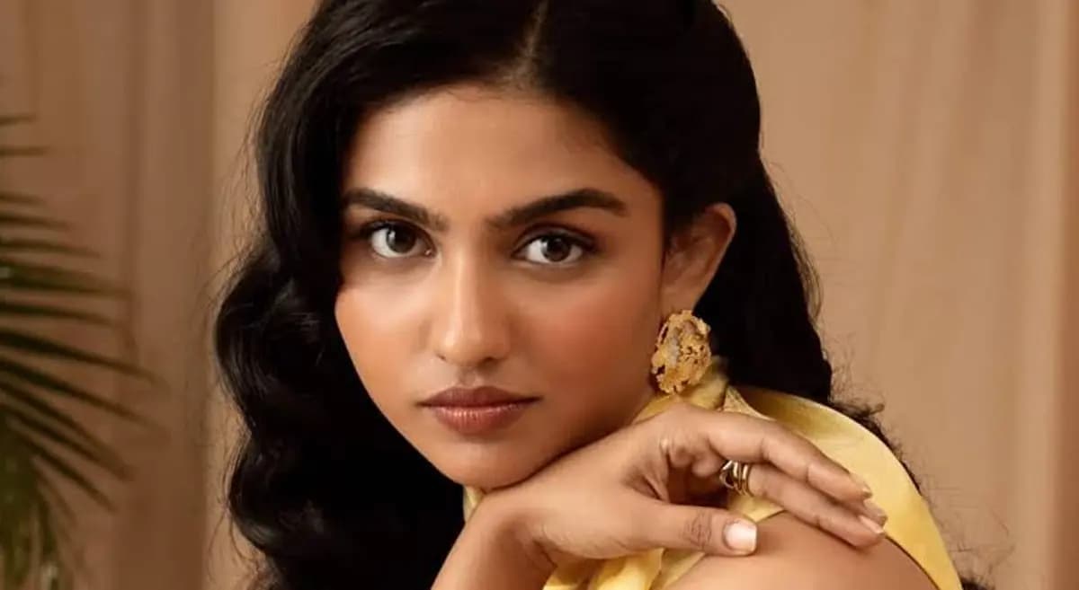 Mamitha Baiju standing confidently in front of a glowing screen displaying Netflix and JioHotstar logos, symbolizing her dual chart-topping success.