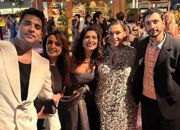 Huma Qureshi at the Emmys, dressed in a sleek black gown, standing beside Riz Ahmed who smiles beside her.