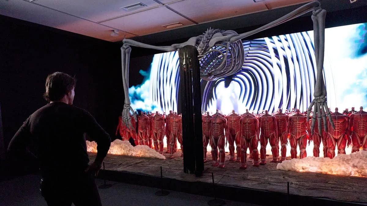 Tom Cruise standing in front of a large animated display of Titans destroying a city, looking thoughtful.