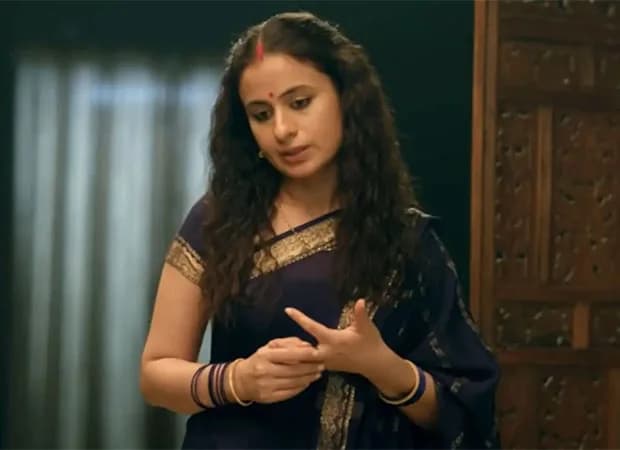 Rasika Dugal as Beena Tripathi standing in a dimly lit room, looking contemplative, with the Mirzapur logo blurred in the background.