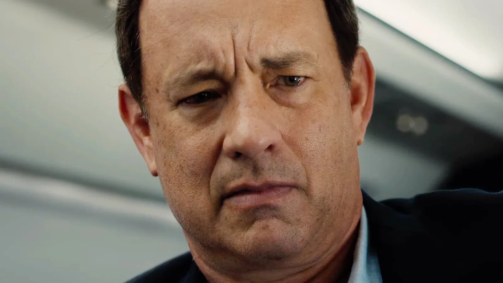Tom Hanks in a suit, standing in front of a cathedral, looking serious. The background is blurred, but the architecture is unmistakable.