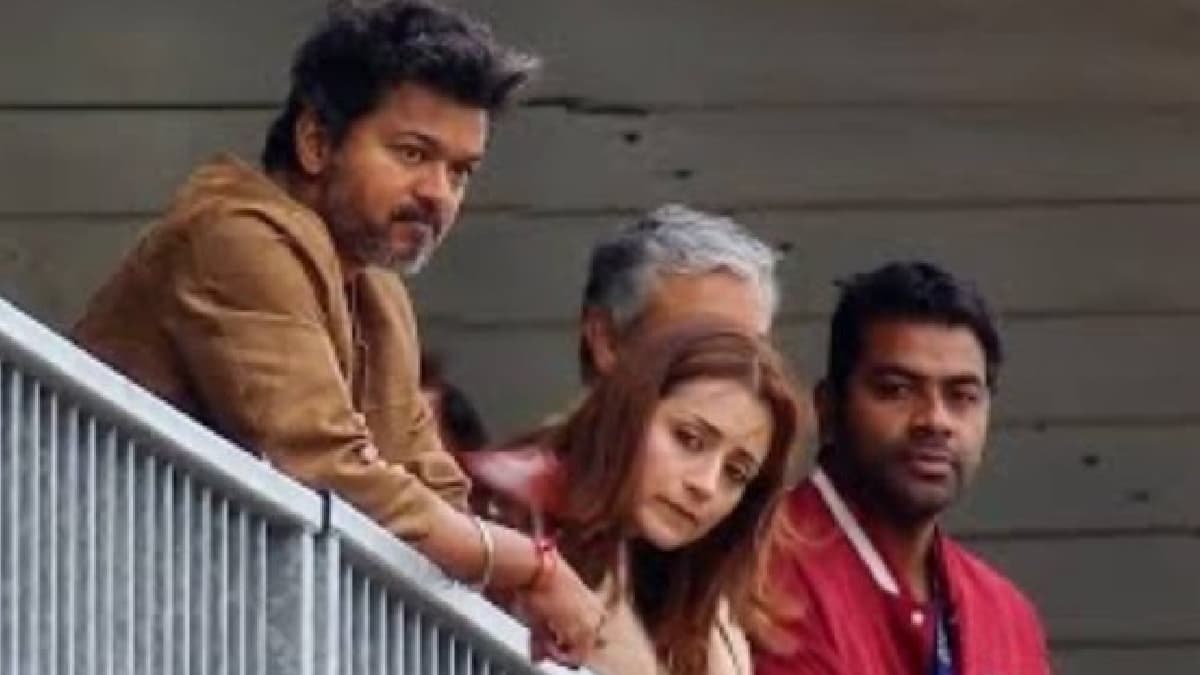 Vijay and Trisha Krishnan seated in the stands at Silverstone Circuit watching a race, with Vijay partly turned away from the camera.
