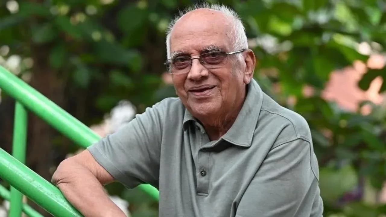 Black-and-white photo of a frail but sharp-eyed man in a white shirt, seated in a chair, looking directly into the camera. A faint smile. The words 'Singeetham Srinivasa Rao' etched below.