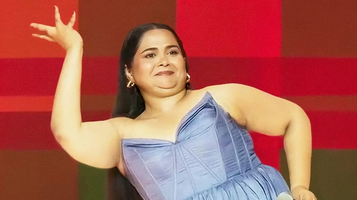 Sumukhi Suresh on stage during her stand-up special Hoemonal, performing under spotlight with audience in background.