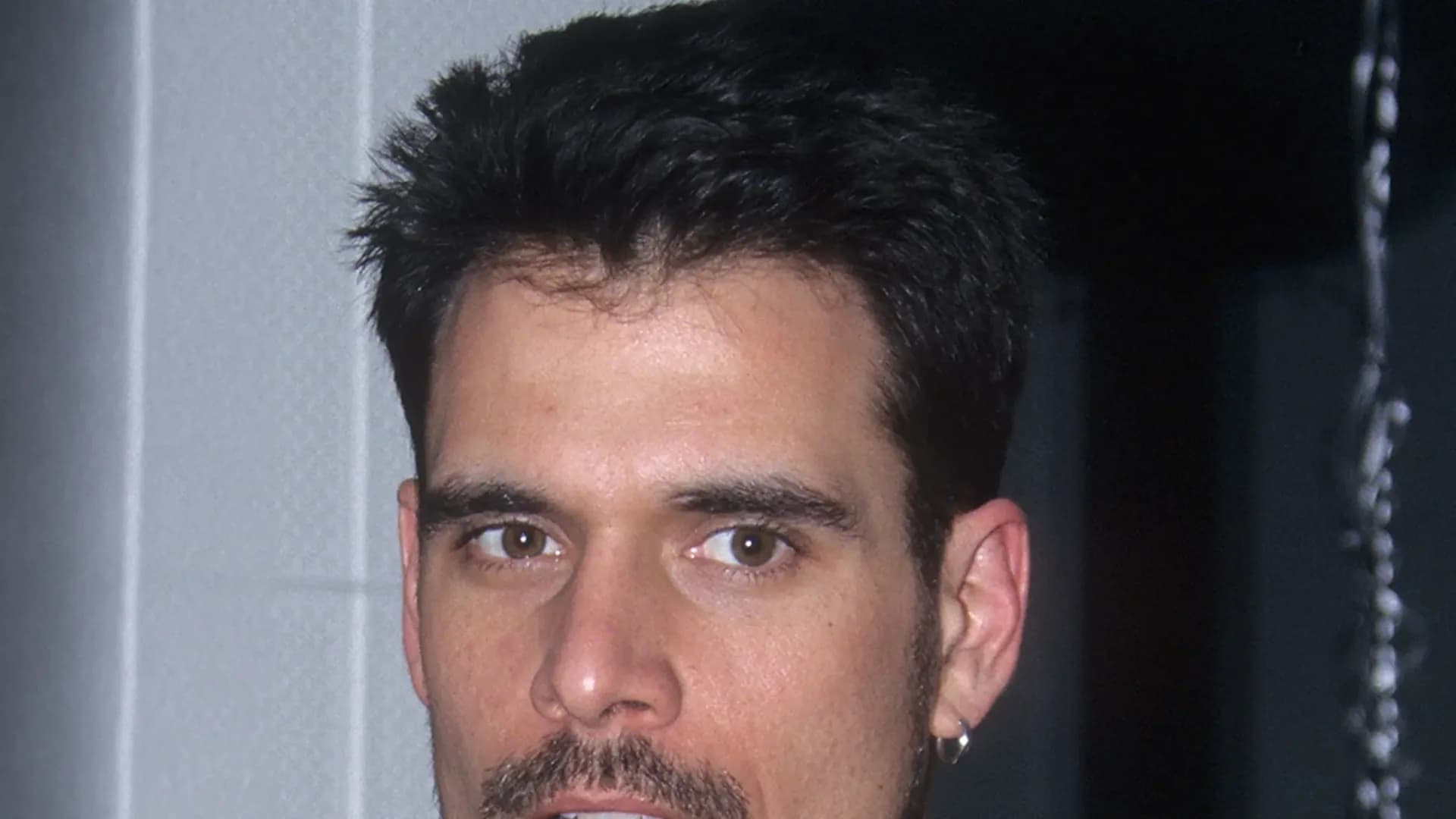 A black-and-white photo of Robert Kelker-Kelly in profile, wearing a dark shirt, looking toward the camera with a calm expression.
