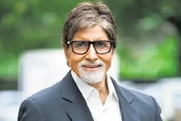 Amitabh Bachchan sitting on a chair during a KBC 18 episode, pointing to his left knee.
