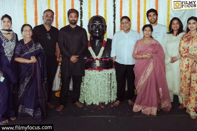 Allu Arjun standing in front of a modern office building with a sign that reads 'ICONZA', smiling with family members beside him.