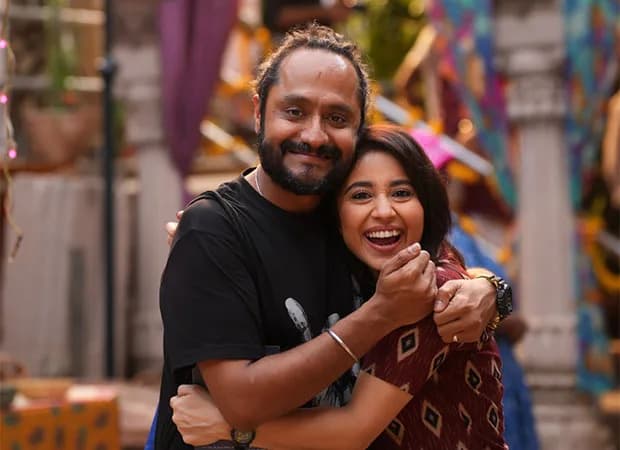 Shweta Tripathi in a bold red saree, standing in front of a stylized Mirzapur sign, smiling at the camera
