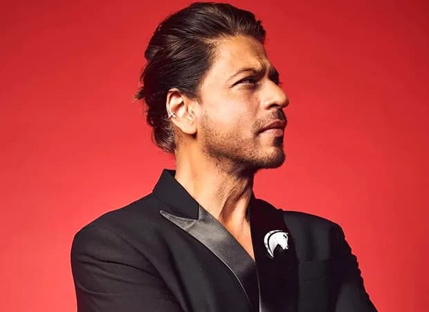 Shah Rukh Khan in a dramatic pose, mid-action, against a dark city skyline