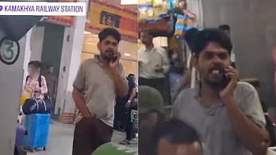 A man in a grey polo shirt and brown shorts standing on a railway platform, seen through a train window at Kamakhya railway station.