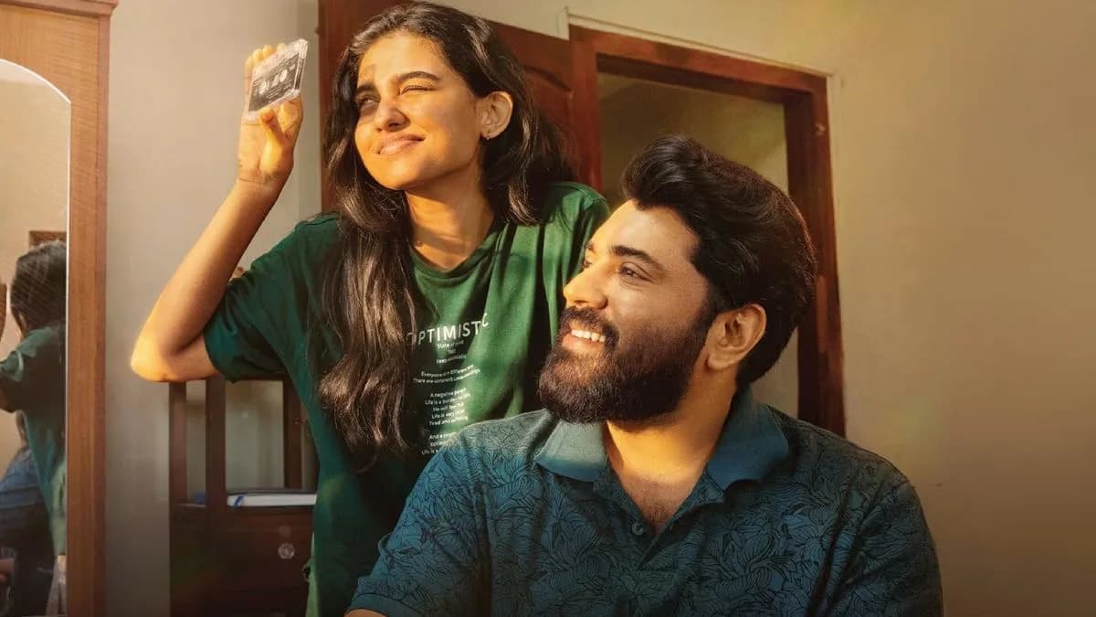 Nivin Pauly and Mamitha Baiju in a warm embrace, standing in front of a colorful neighborhood house.