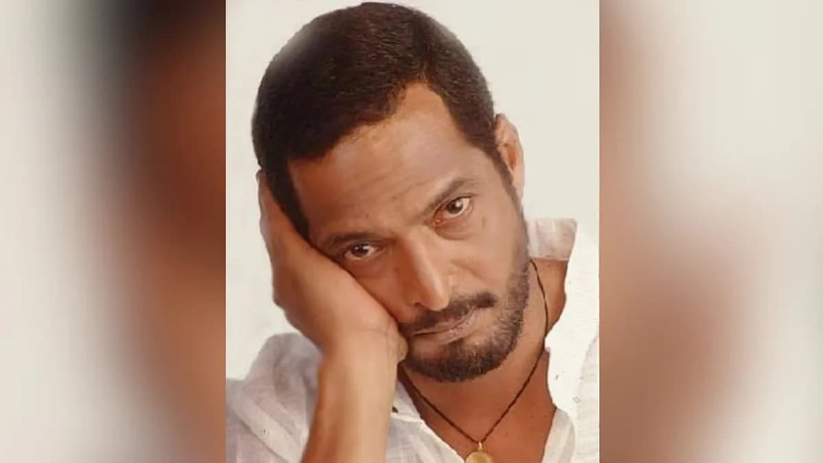 Nana Patekar in a black coat, standing in front of a grey wall, looking directly into the camera with a serious expression.
