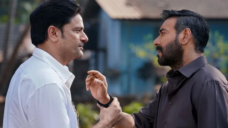 Ajay Devgn in a tense scene from Drishyam The Conclusion, eyes locked on the camera, shadows falling across his face.