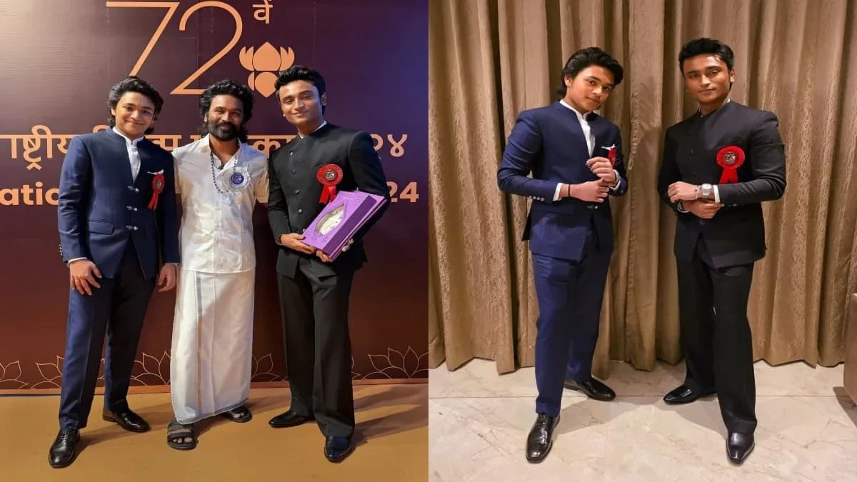 Actor Dhanush smiling while posing with his National Film Award trophy alongside his two sons