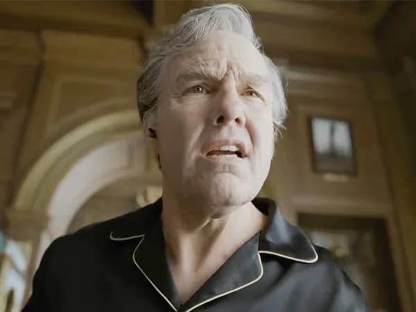 Tom Cruise in a dark, surreal scene from Digger, standing in a vast empty space with a single spotlight on him.