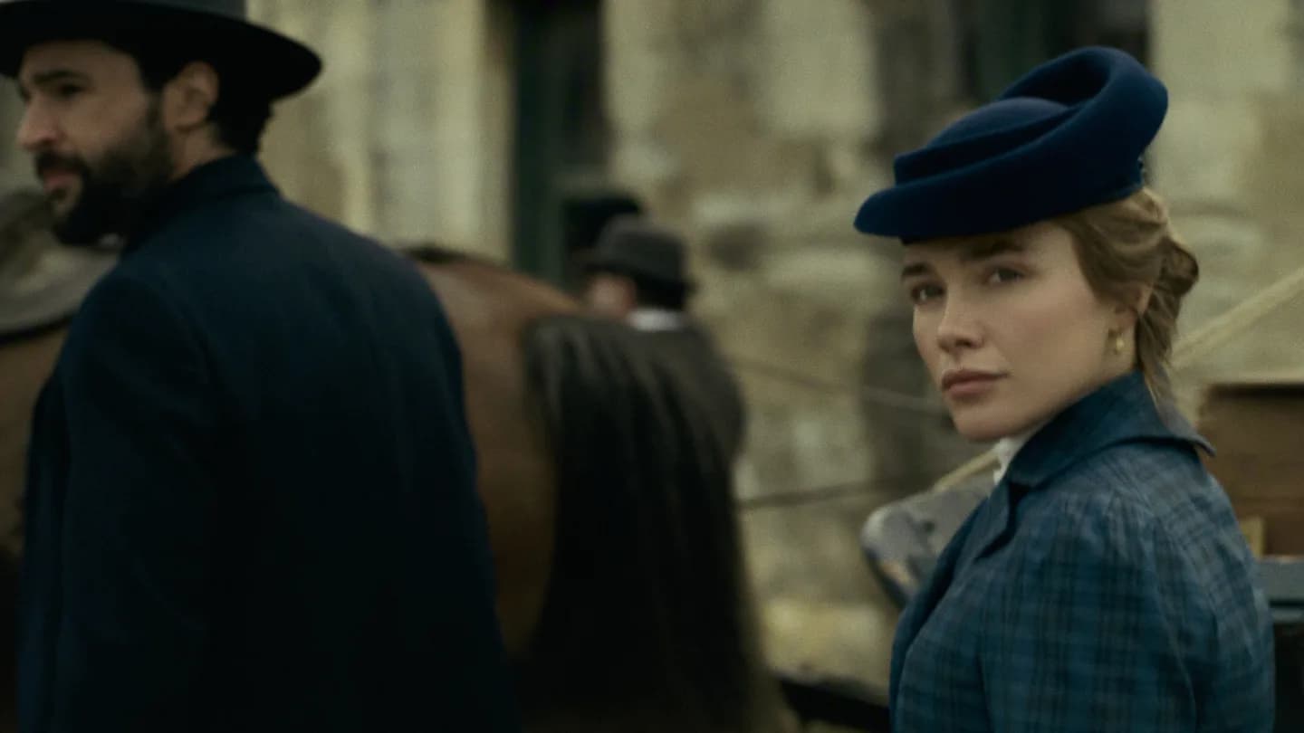 Florence Pugh in a dramatic close-up, eyes intense, standing in a dimly lit room.
