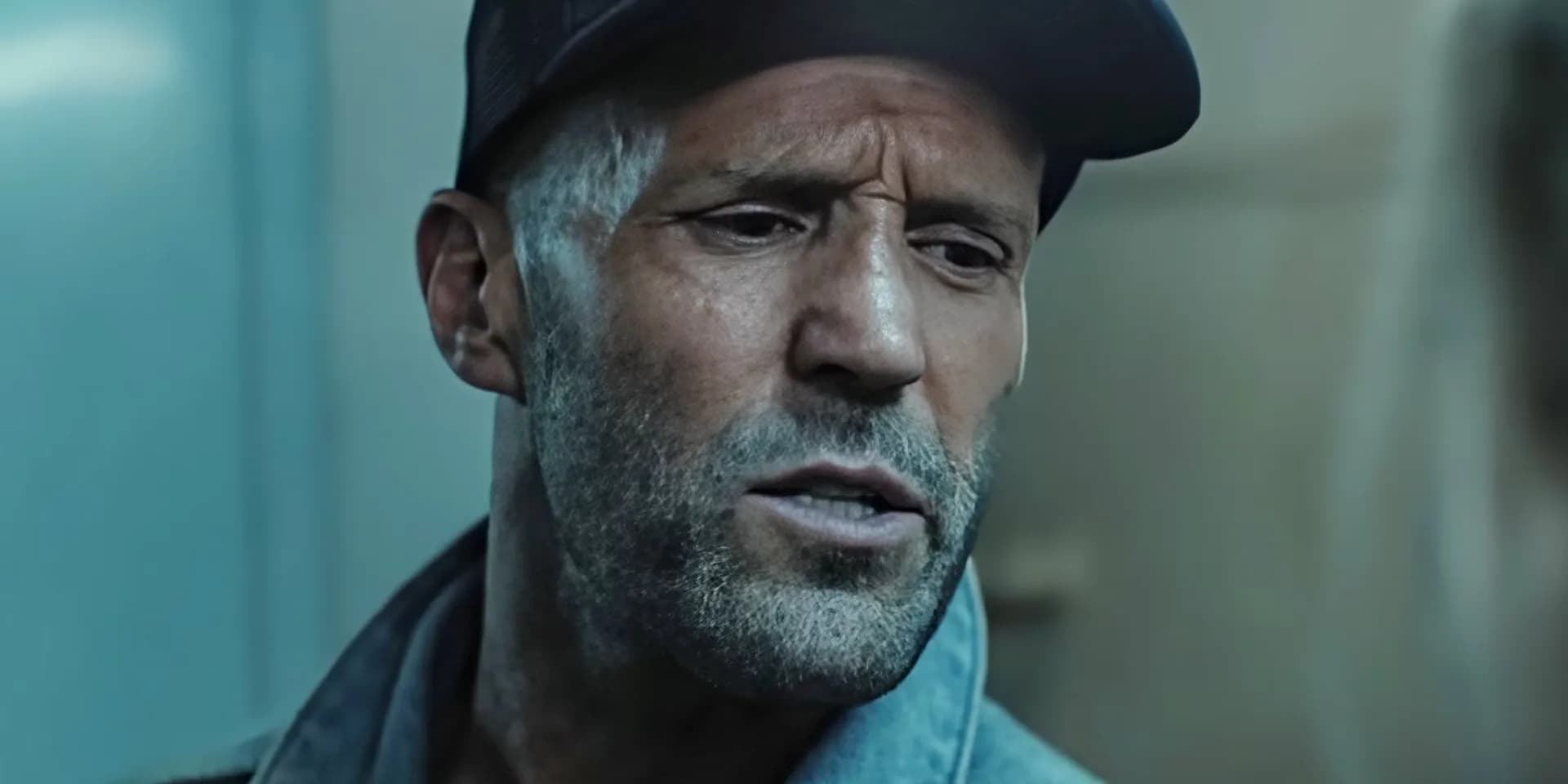 Jason Statham in a dark coat, standing on a ship deck, looking tense amid stormy skies