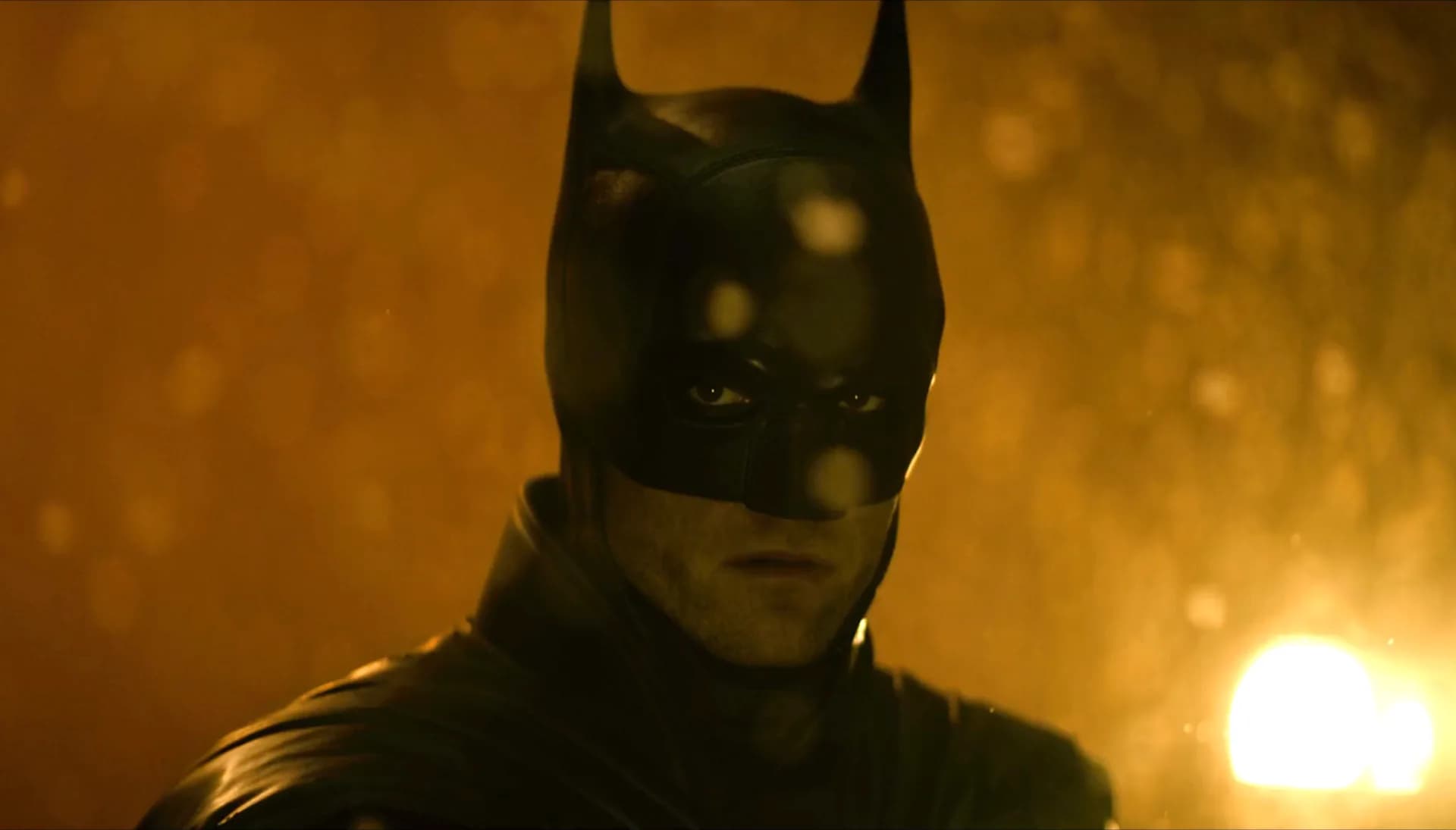 Robert Pattinson in full Batman suit, standing in rain-drenched Gotham street, eyes hidden behind cowl.