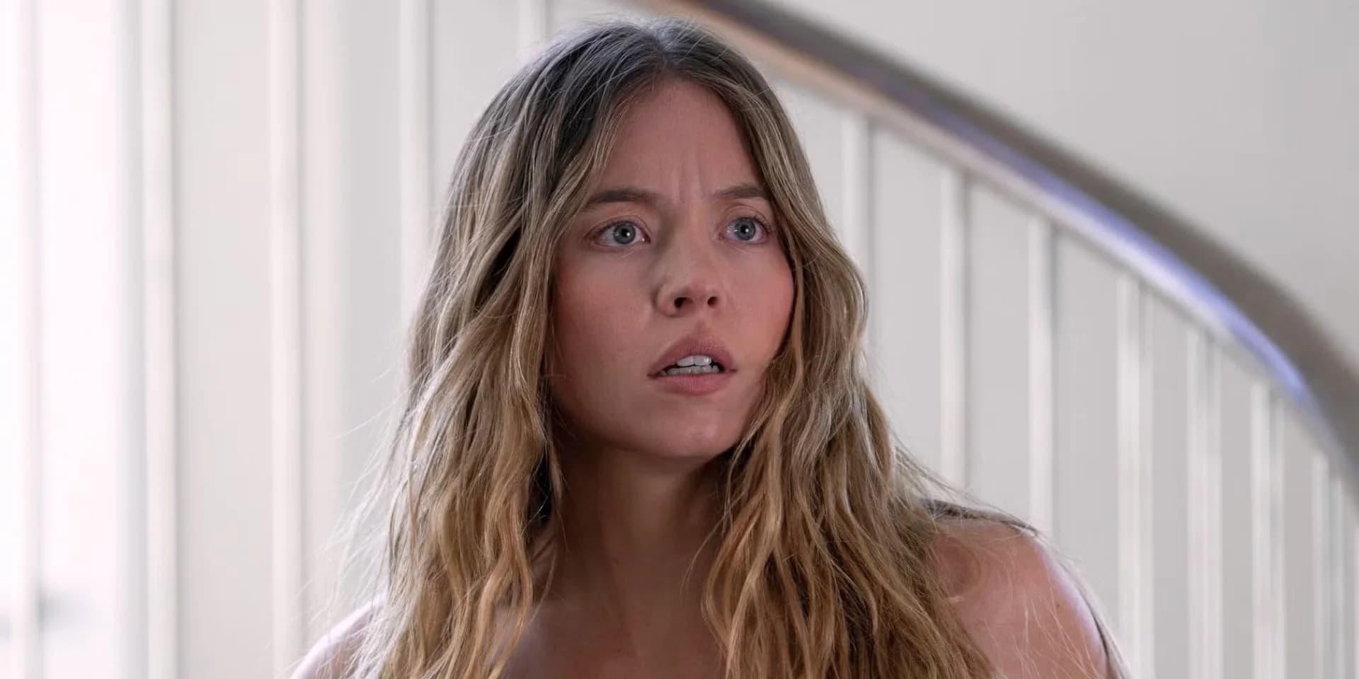 Sydney Sweeney in a tense scene from The Housemaid, face lit by dim light, eyes wide with fear.
