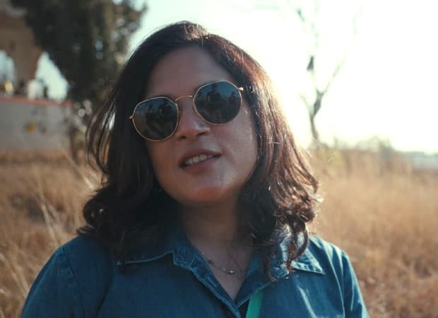 Richa Chadha standing near the hexagonal Gilbert Hill in Andheri, Mumbai, holding a camera and looking up at the temple atop the rock.