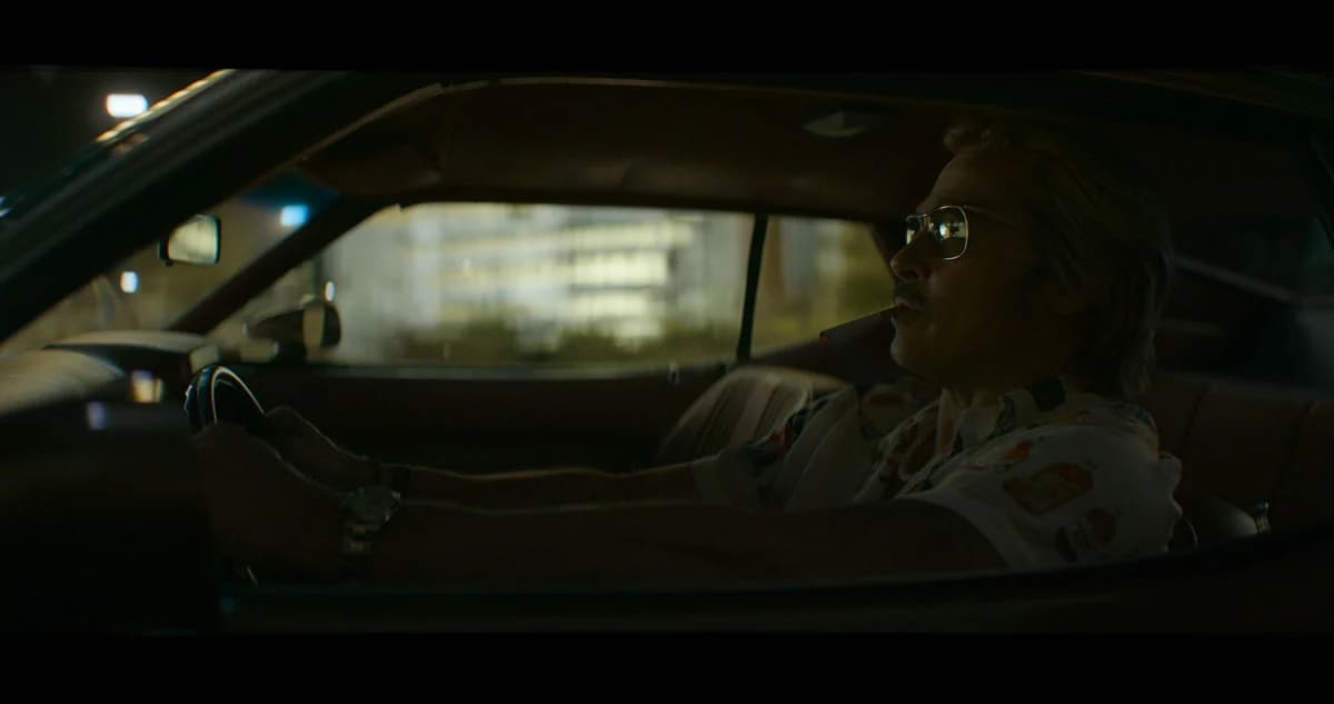 Brad Pitt as Cliff Booth standing in front of a neon‑lit Beverly Cinema, trailer screenshot