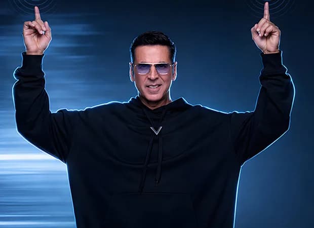 Akshay Kumar standing in front of a modern home setup featuring Acer-branded appliances like a TV, washing machine, and laptop.