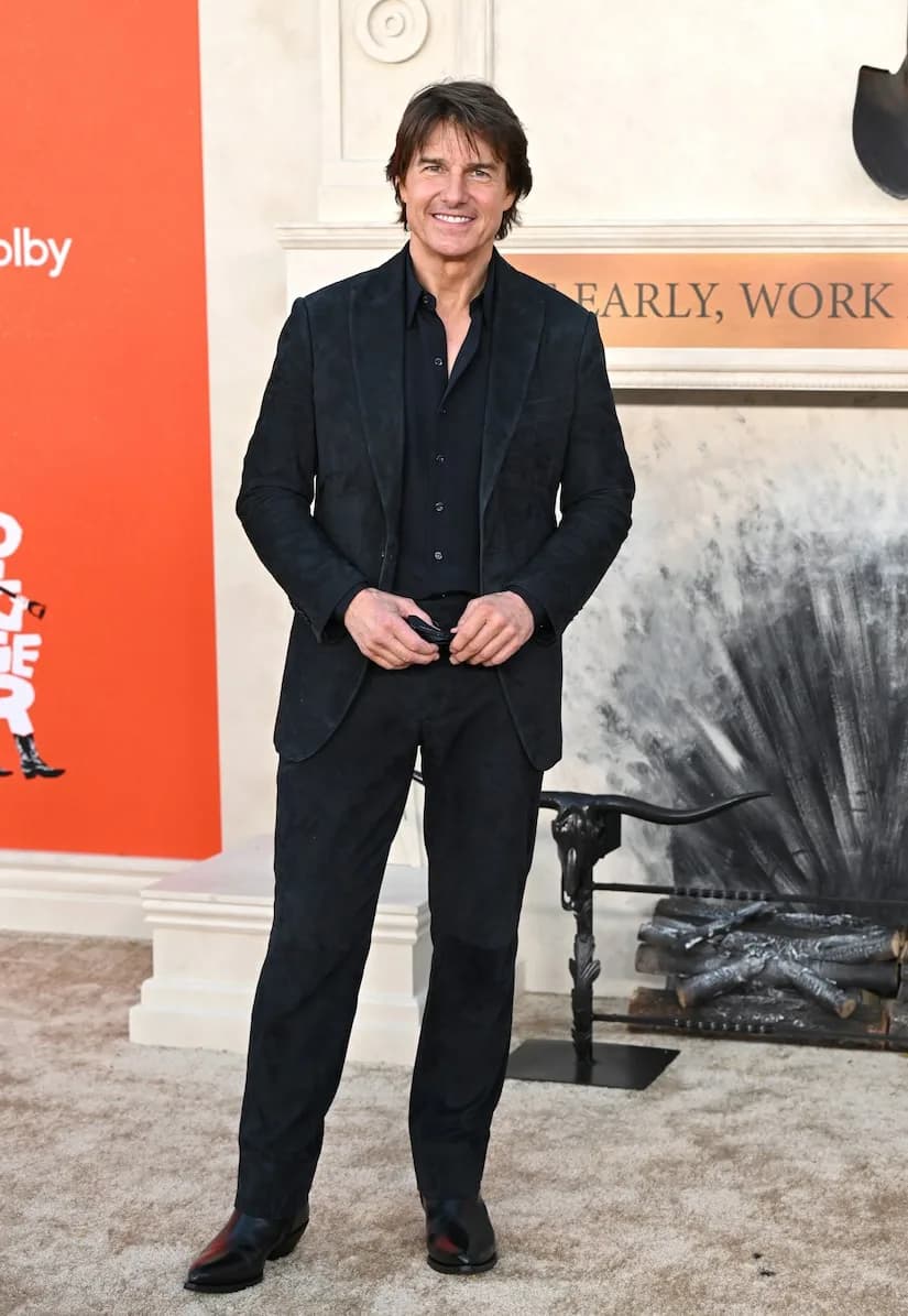 Tom Cruise standing on the red carpet at the Los Angeles premiere of Digger, smiling beside a portrait of Kate Middleton.
