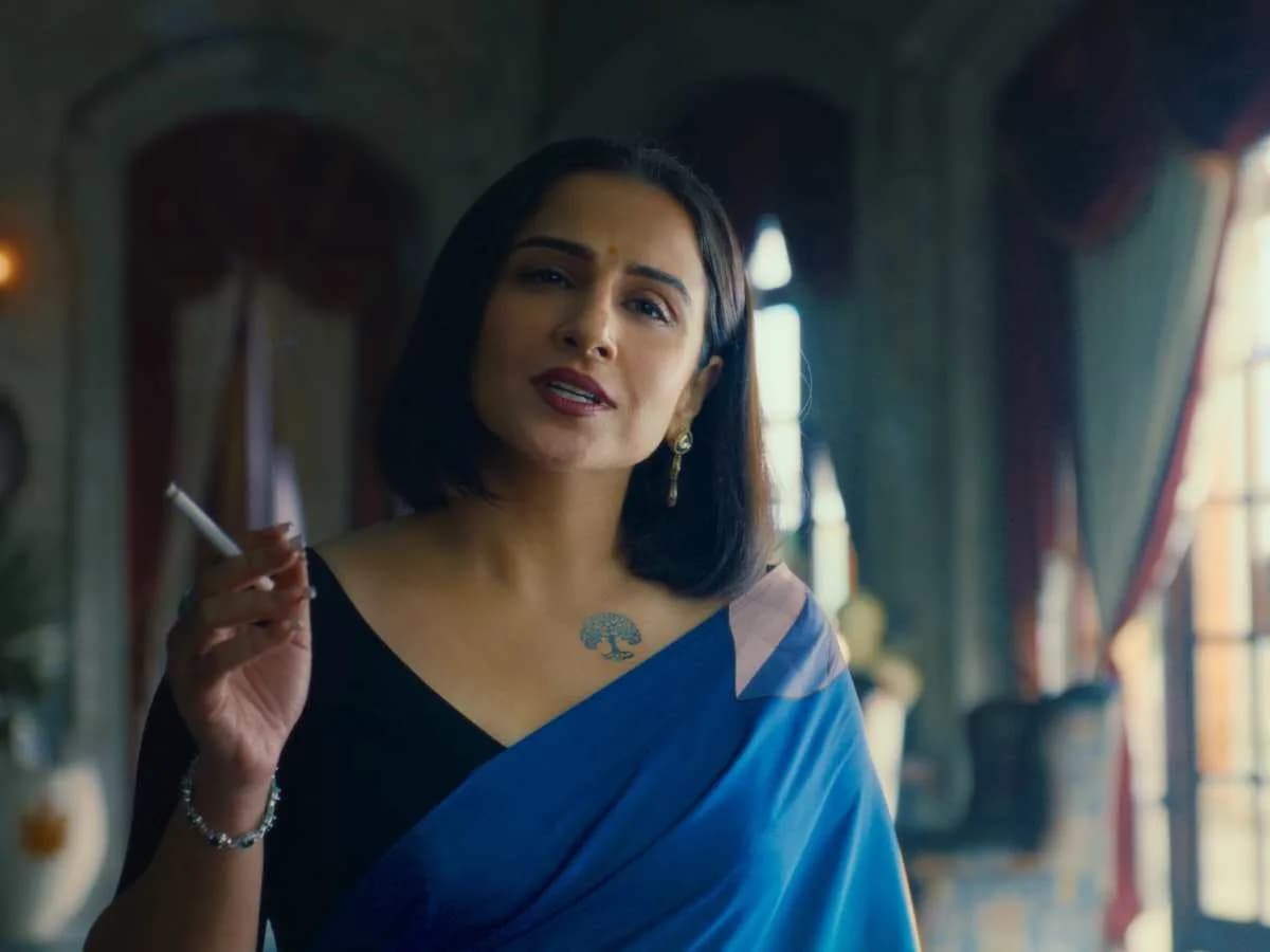 Vidya Balan in a dramatic pose, eyes sharp, holding a cigarette, smoke curling toward the camera.