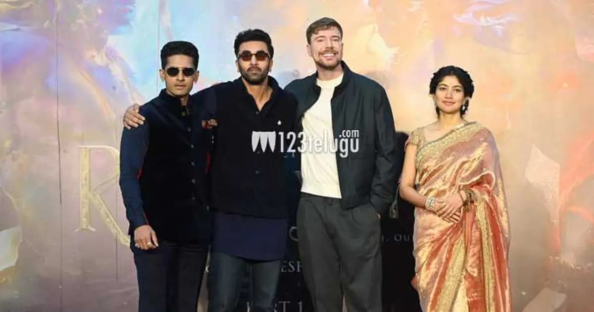 MrBeast standing beside the Ramayana poster at a promotional event in Kerala, surrounded by crew and Indian officials