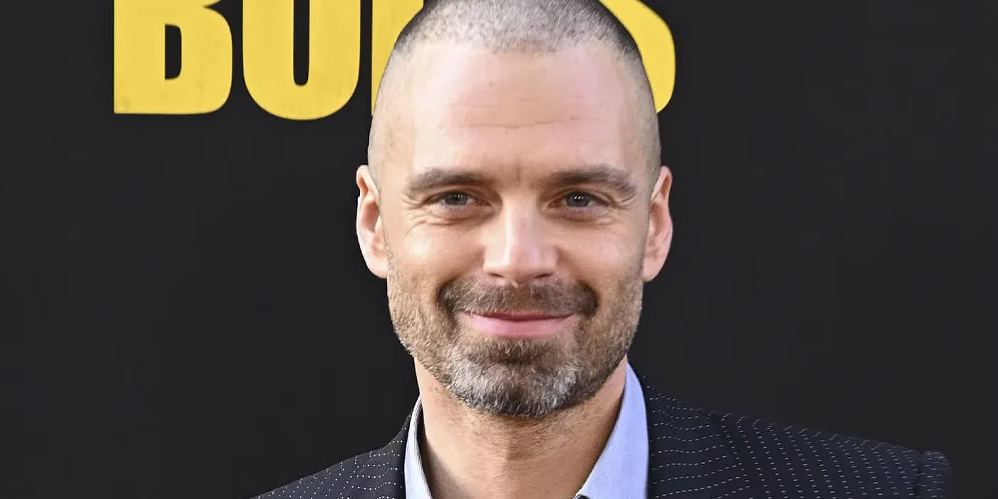 Sebastian Stan in a close-up shot, bald on top, sideburns thick, wearing glasses, looking directly at the camera with intensity.
