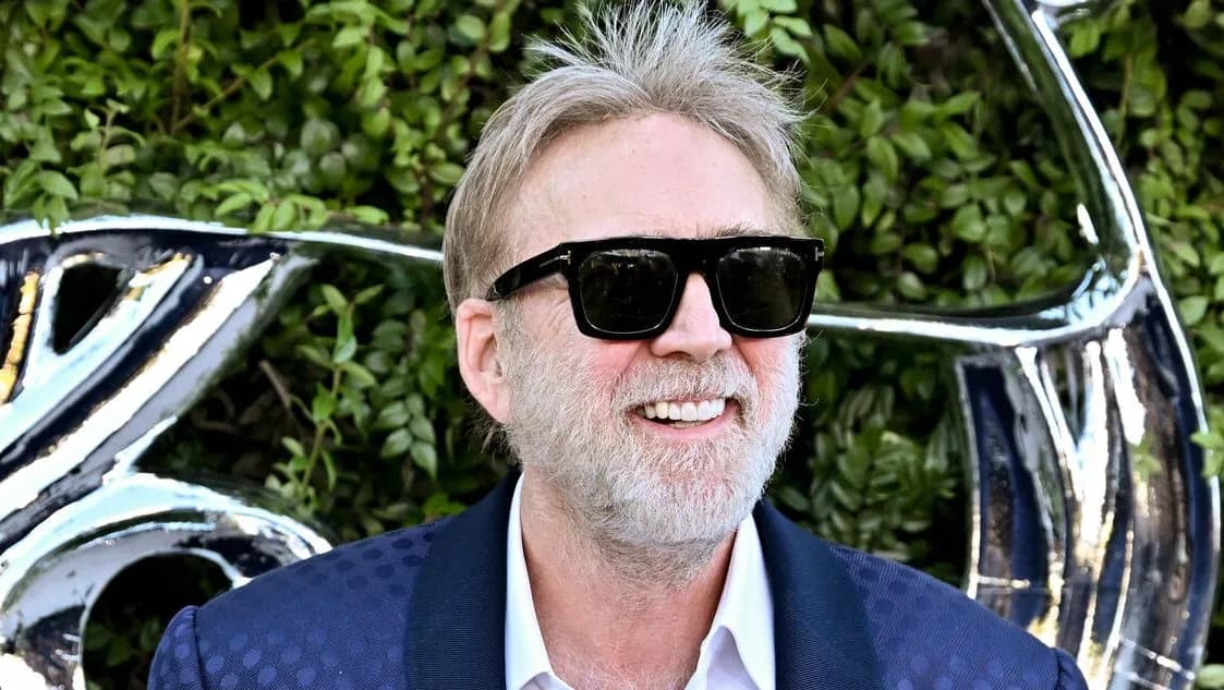 Nicolas Cage at Fan Expo Dallas, holding a microphone, looking serious.