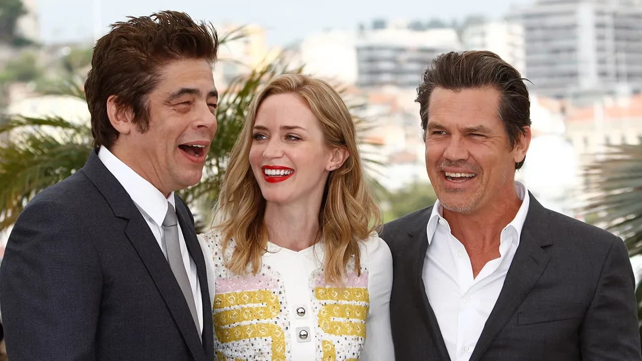A still from the original Sicario featuring Emily Blunt, Benicio Del Toro, and Josh Brolin standing in a tense, shadowed corridor.