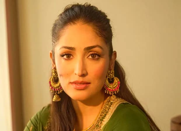 Yami Gautam Dhar in a dramatic pose, wearing a traditional yet fantastical outfit, standing in front of a surreal backdrop.