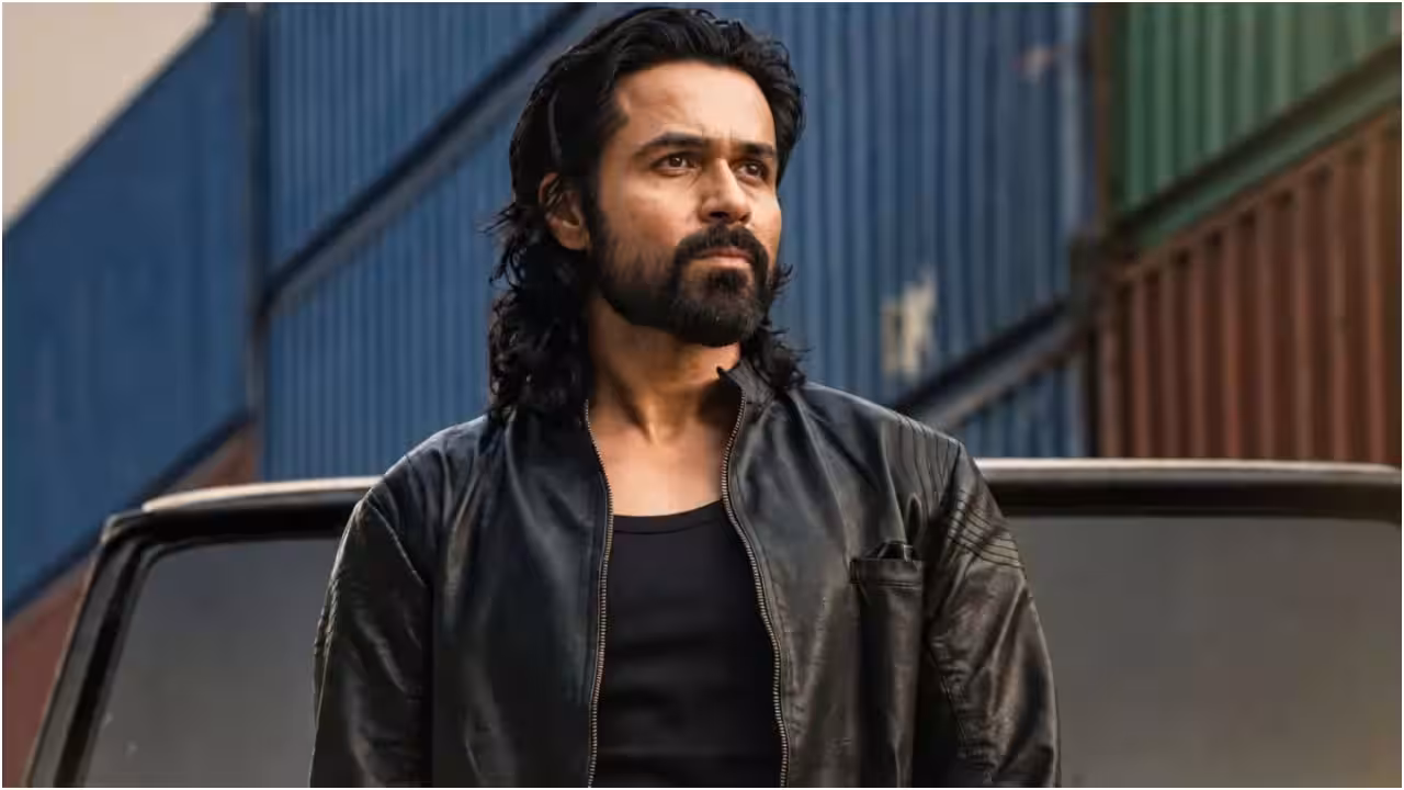 Emraan Hashmi in a dark coat, standing in a rain-soaked alley, looking over his shoulder. The sky is grey. The title 'Awarapan 2' glows faintly in red.