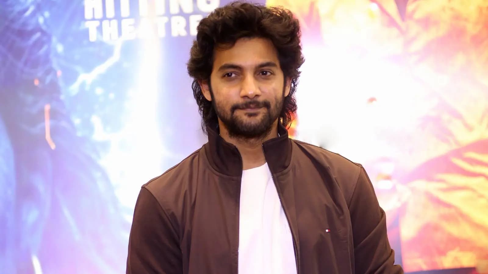 Aadi Saikumar speaking into a microphone, standing in front of a city skyline