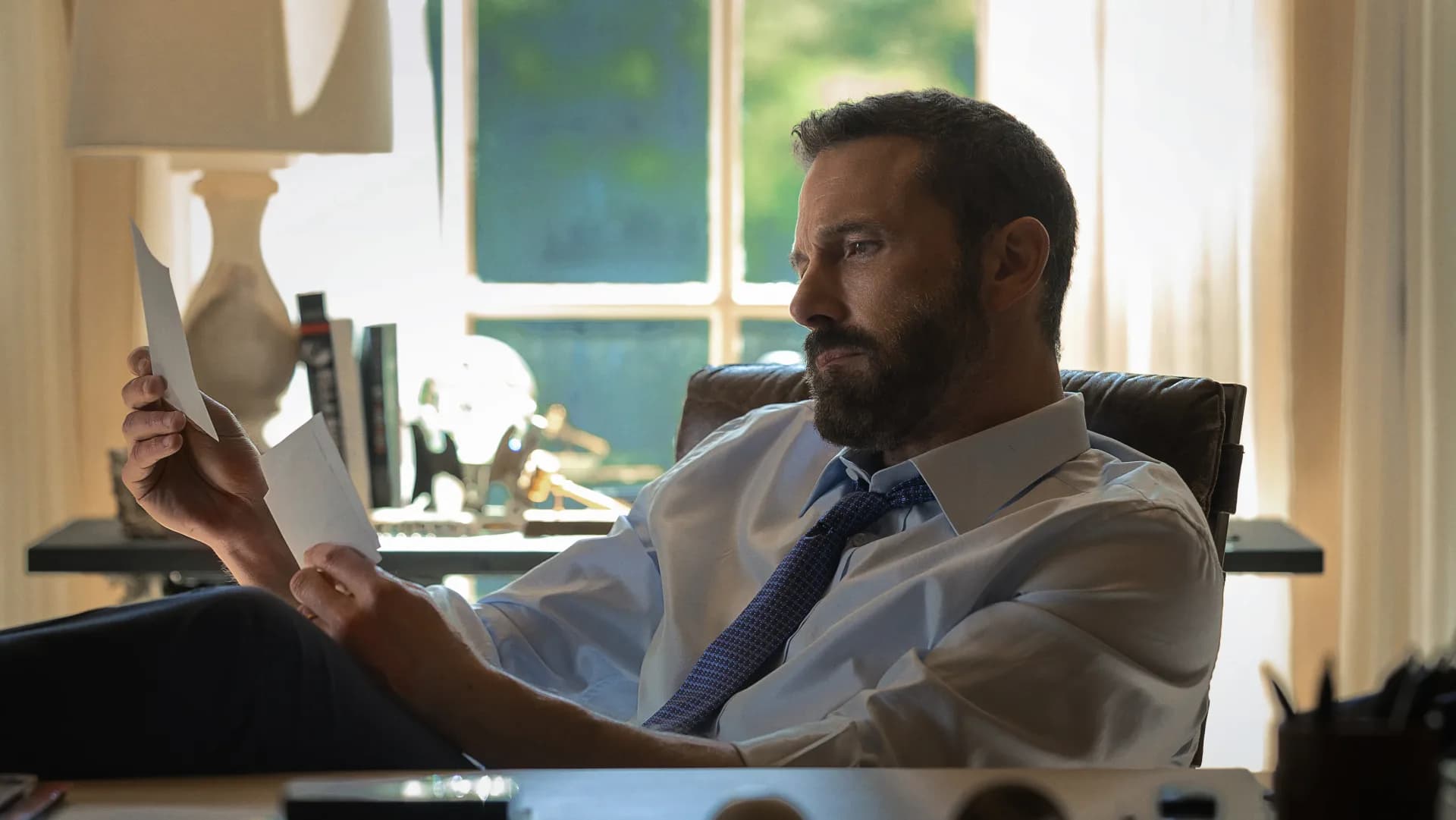 Ben Affleck in a suit, looking serious, standing in front of a city skyline.